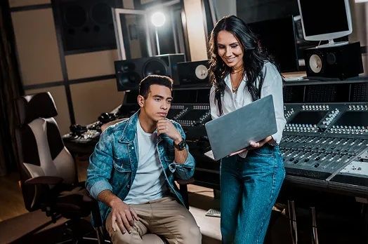 Zwei Personen prüfen in einem Tonstudio Audiodaten auf einem Laptop